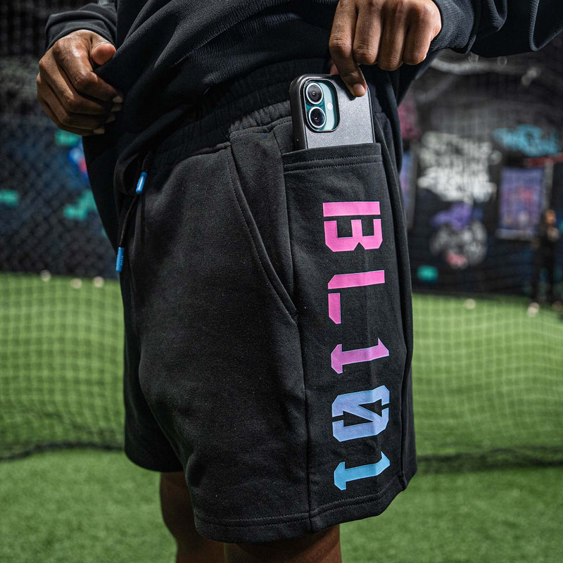 Person wearing black shorts with colorful BL101 text, holding a phone, on a sports field.