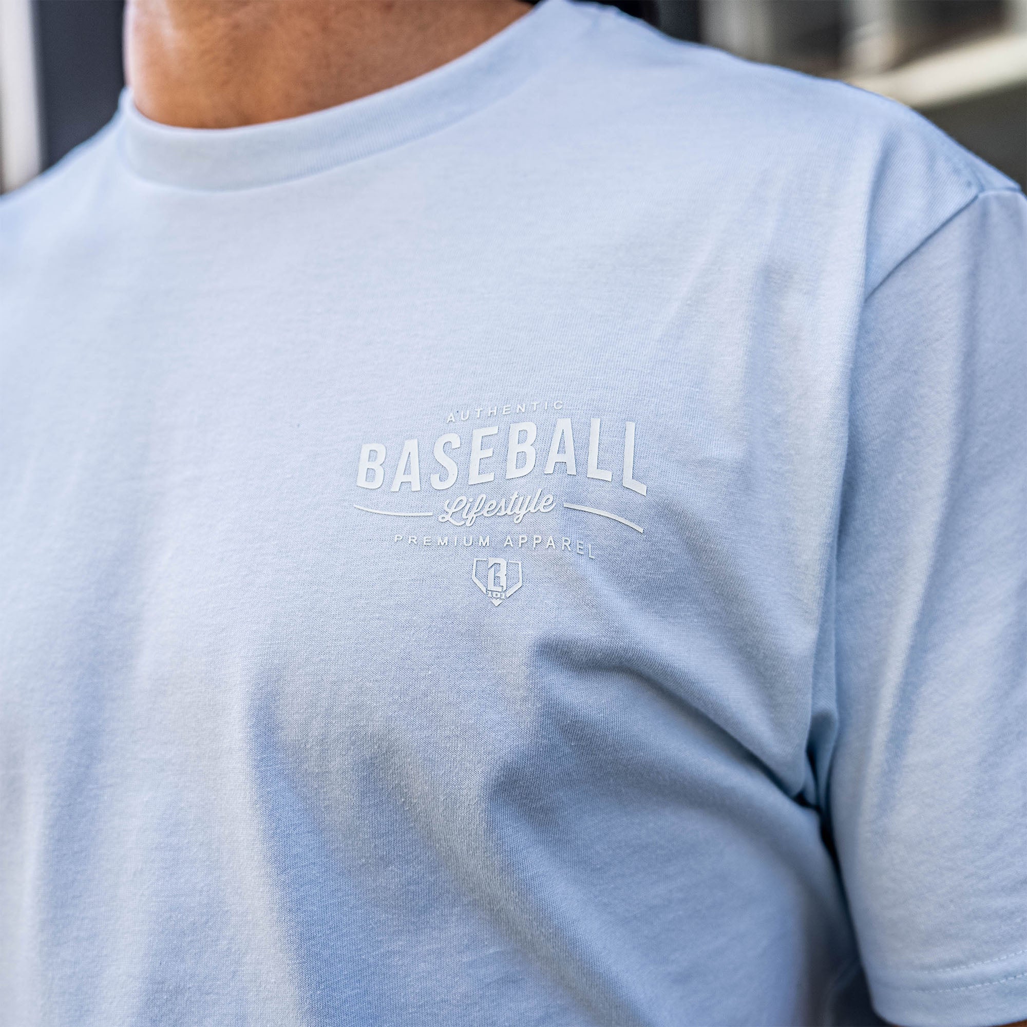 Light blue t-shirt with 'Authentic Baseball Lifestyle PREMIUM APPAREL' text on a person wearing it.