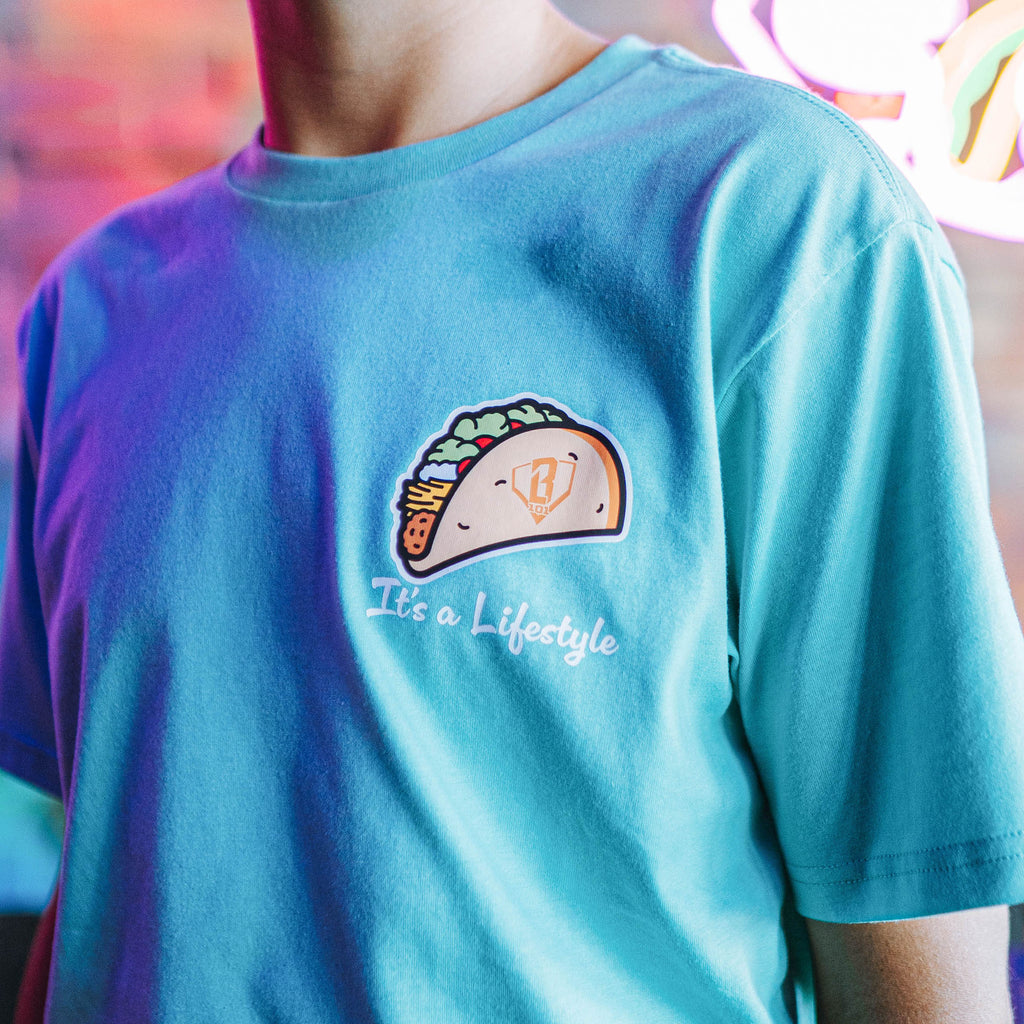 Person wearing teal t-shirt with a taco graphic design and 'It's a lifestyle' text