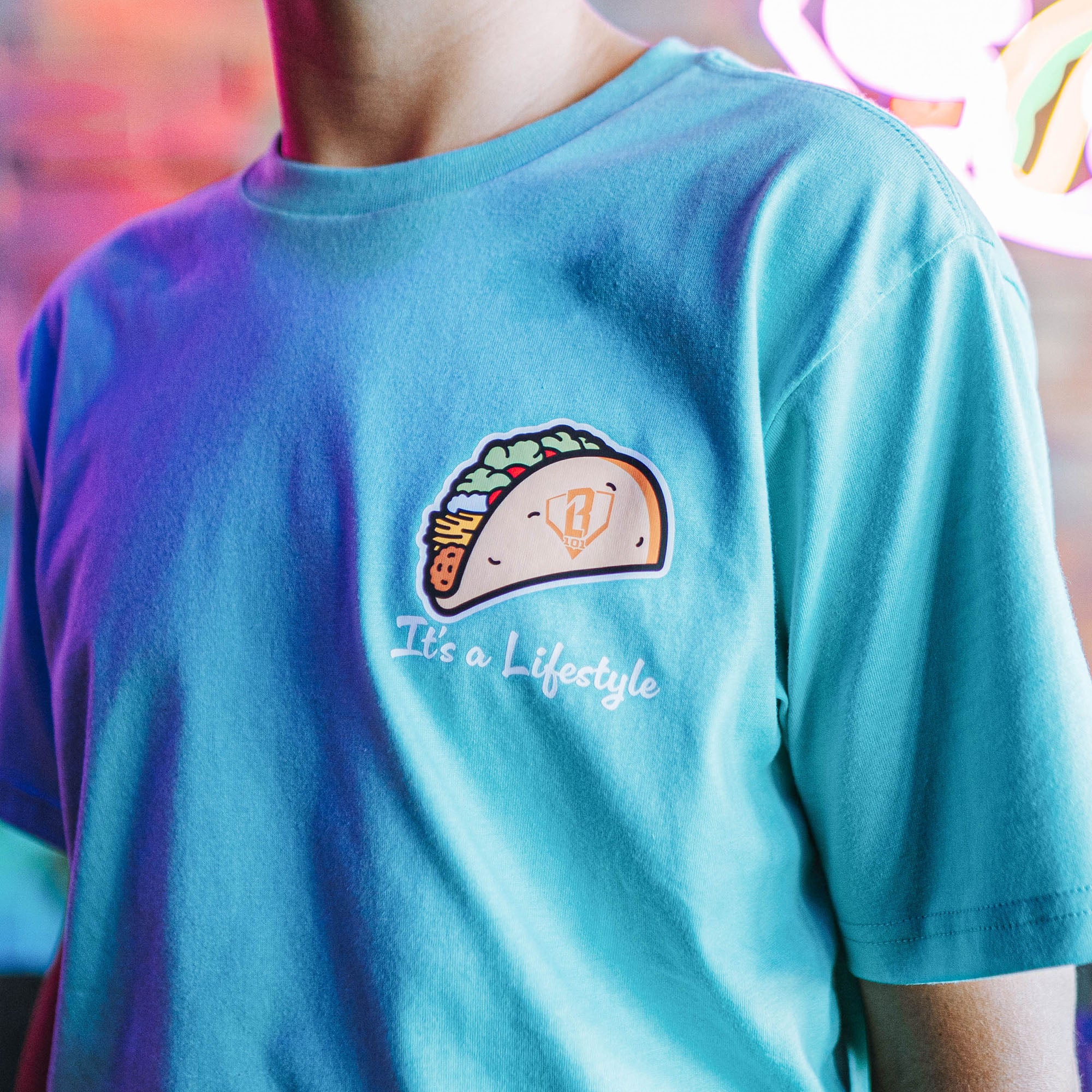 Person wearing teal t-shirt with a taco graphic design and 'It's a lifestyle' text