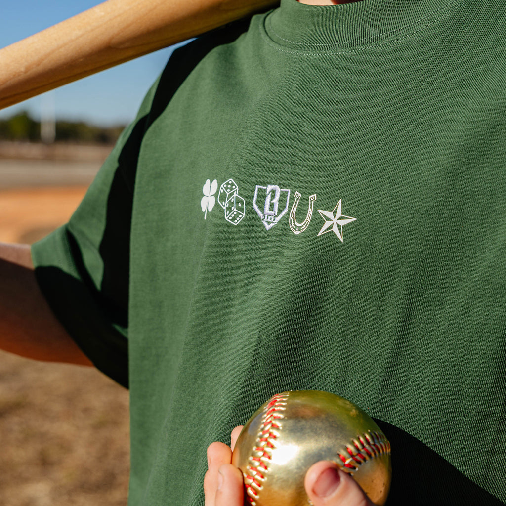 Person wearing a green t-shirt with logos holding a gold baseball on a field.