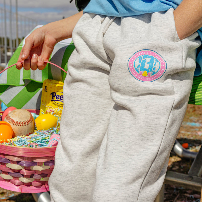 Person wearing gray sweatpants with a colorful BL101 logo, holding an Easter basket with toys and candy.