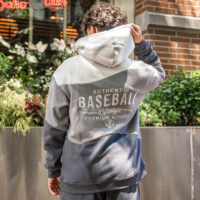 Person wearing a gray and white hoodie with 'Baseball Lifestyle Premium Apparel' text, standing outdoors.