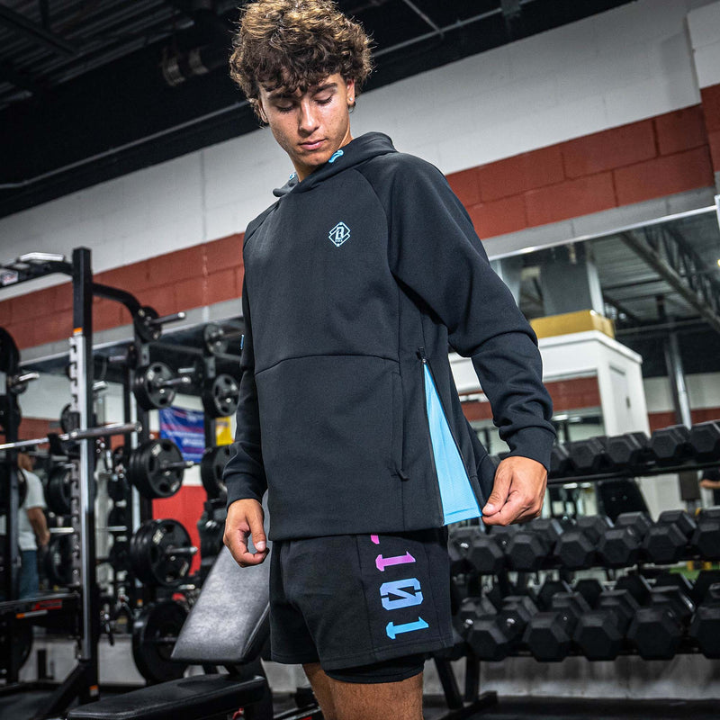 Person wearing a black hoodie and shorts with colorful text in a gym setting