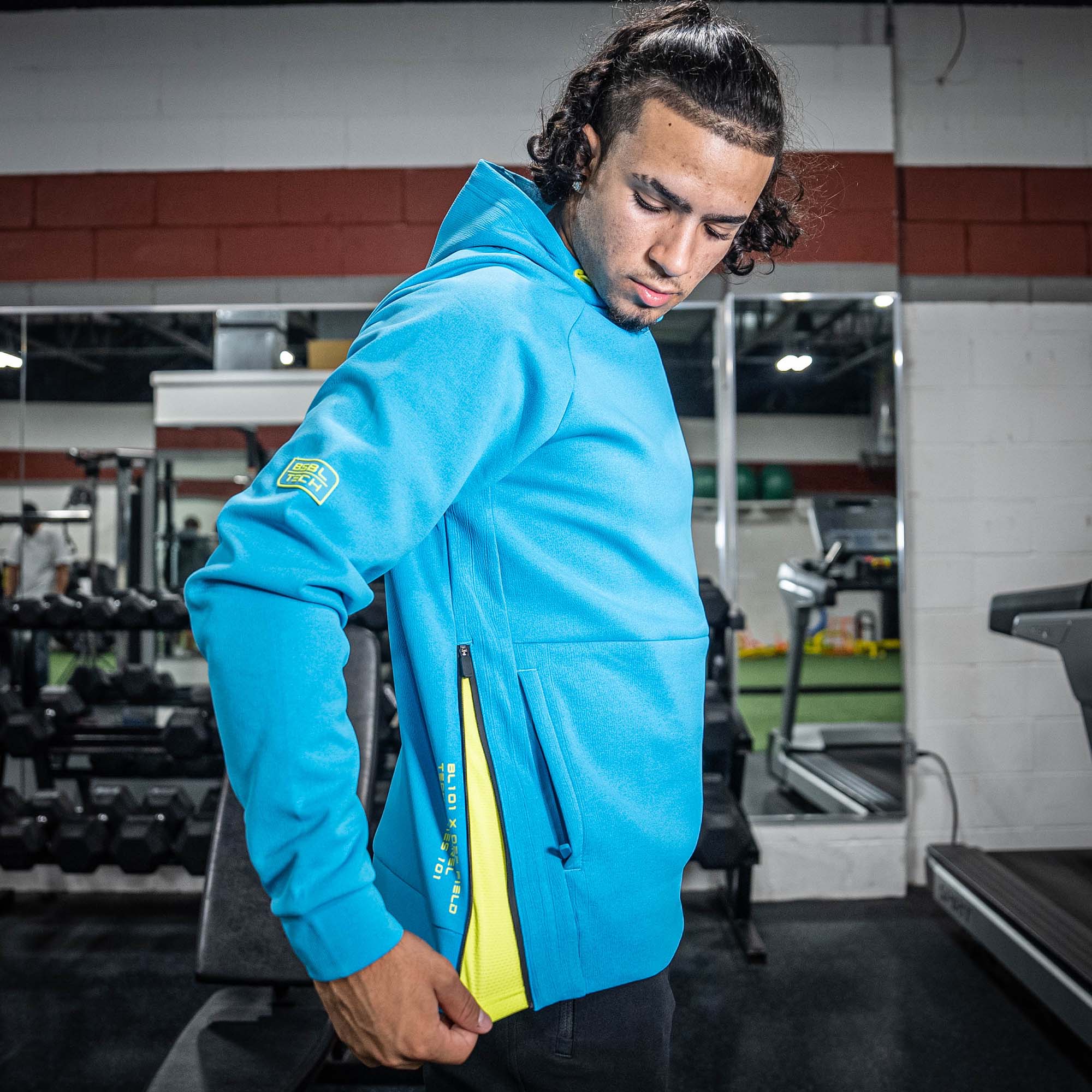Person wearing a blue hoodie with a yellow BL101 logos in a gym setting