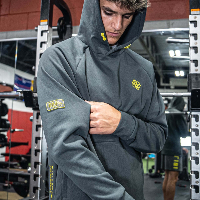 Person wearing a gray hoodie with yellow BL101 logos in a gym setting