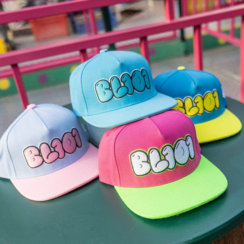 Four colorful caps with 'BL301' text on a green surface, outdoor setting.