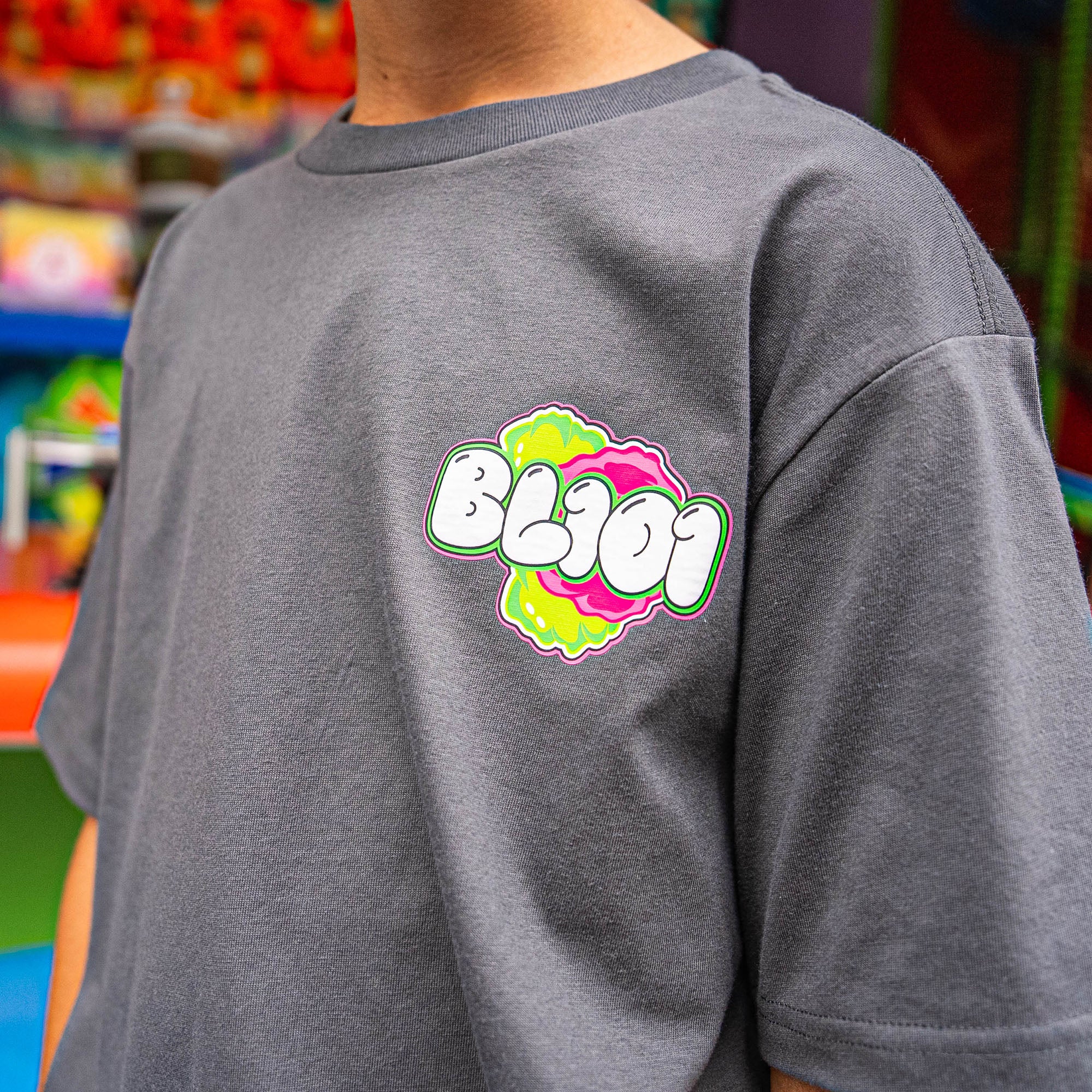 Person wearing a gray t-shirt with a pink and green BL101 logo on the back, in a store setting.
