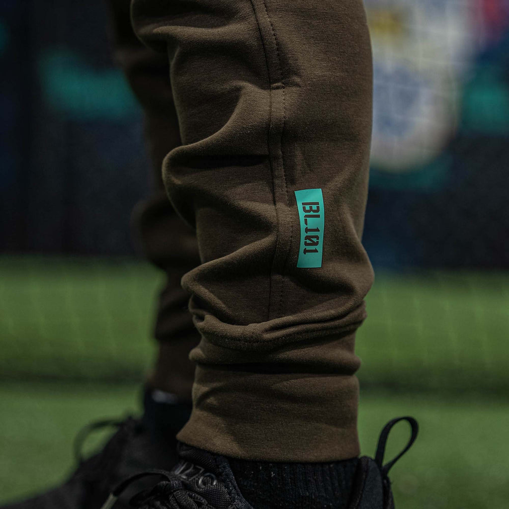 Brown sweatpants with a blue tag on a blurred sports field background