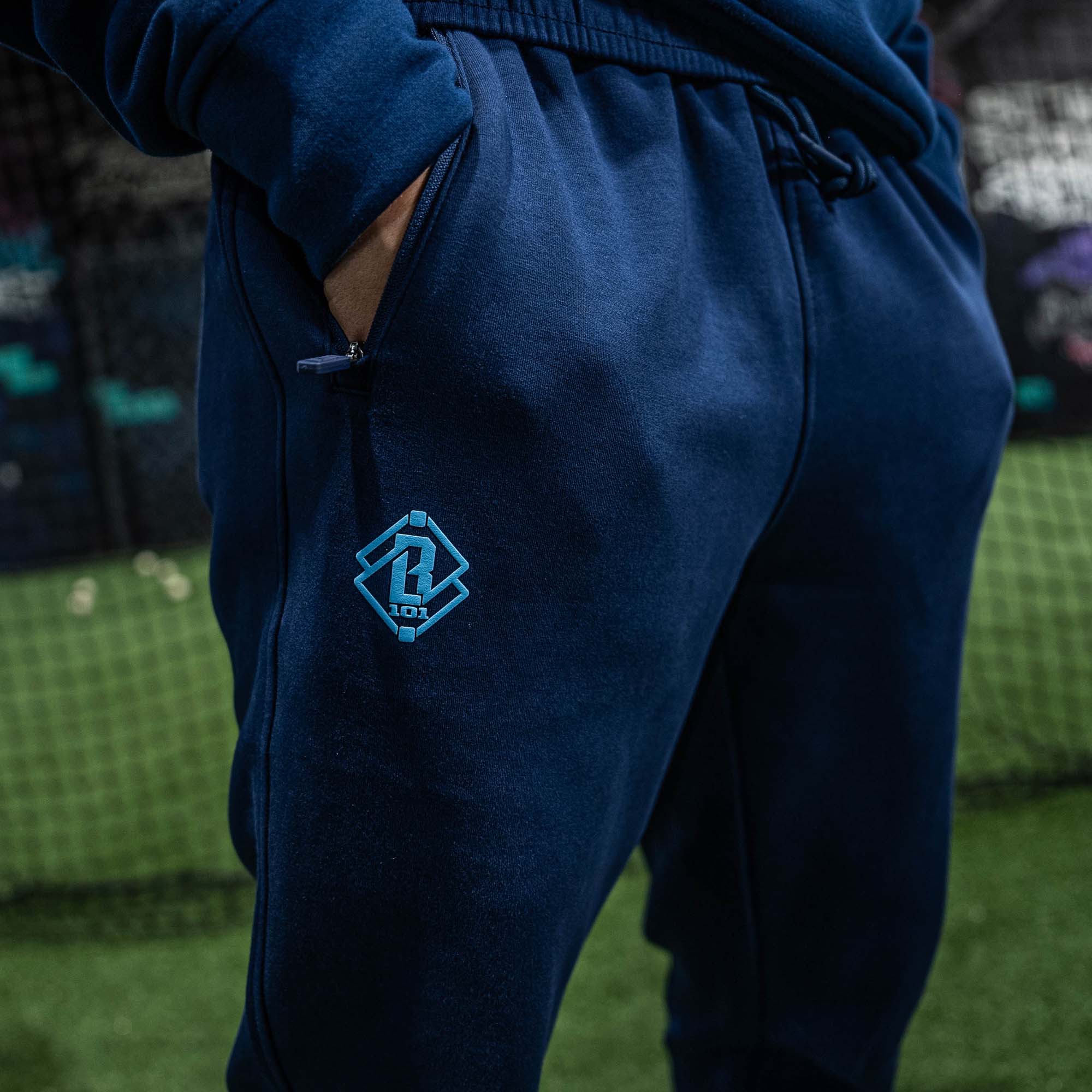Navy blue sweatpants with a small BL101 logo on the leg, worn by a person, against a blurred background.