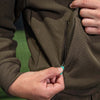 Close-up of a person zipping up a brown jacket with a green background