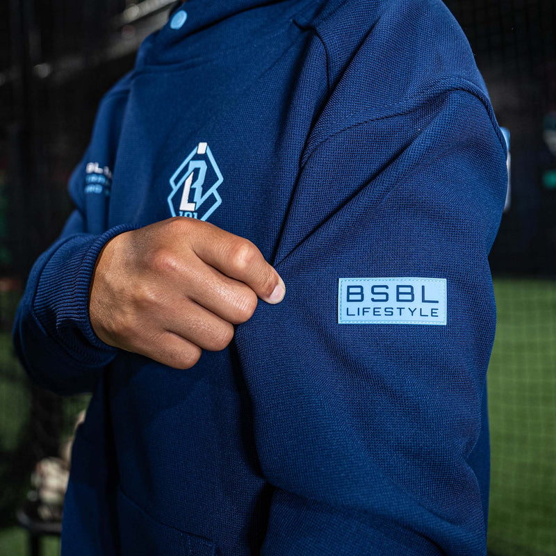 Person wearing a blue hoodie with 'BSBL Lifestyle' branding on a sports field.