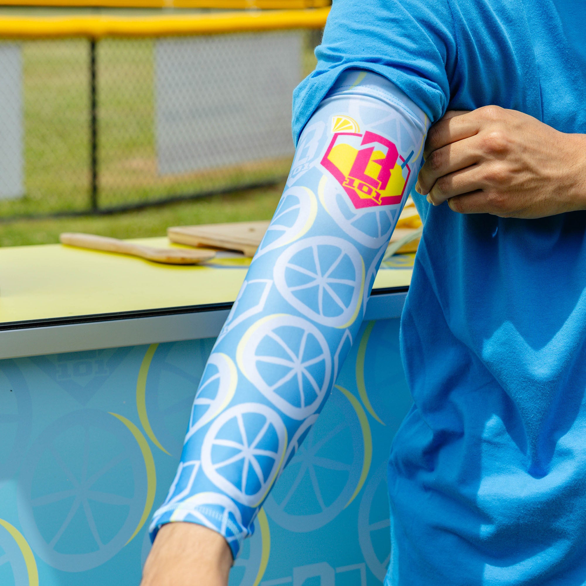 Youth model wearing blue youth arm sleeve with "Lemonade Splash" design