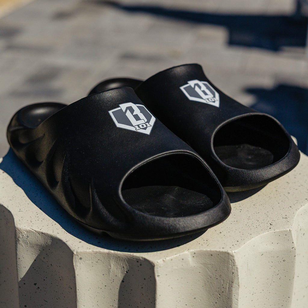 Angled shot of BL101 black slides on a white concrete pedestal with the BL101 logo visible on the strap