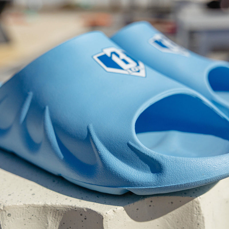 Close-up of BL101 light blue slide showing the textured upper, sculpted sole, and blue home plate logo.