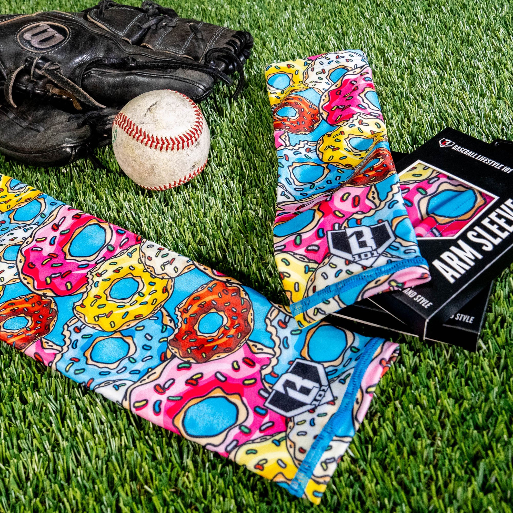 Two donut arm sleeves laid on green turf next to a baseball a glove and the BL101 retail box
