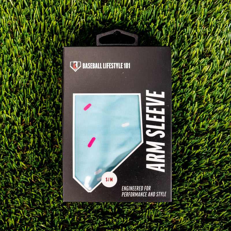 Front of the BL101 arm sleeve retail box on green turf showing the light blue sprinkle print through a home plate window and S/M size label
