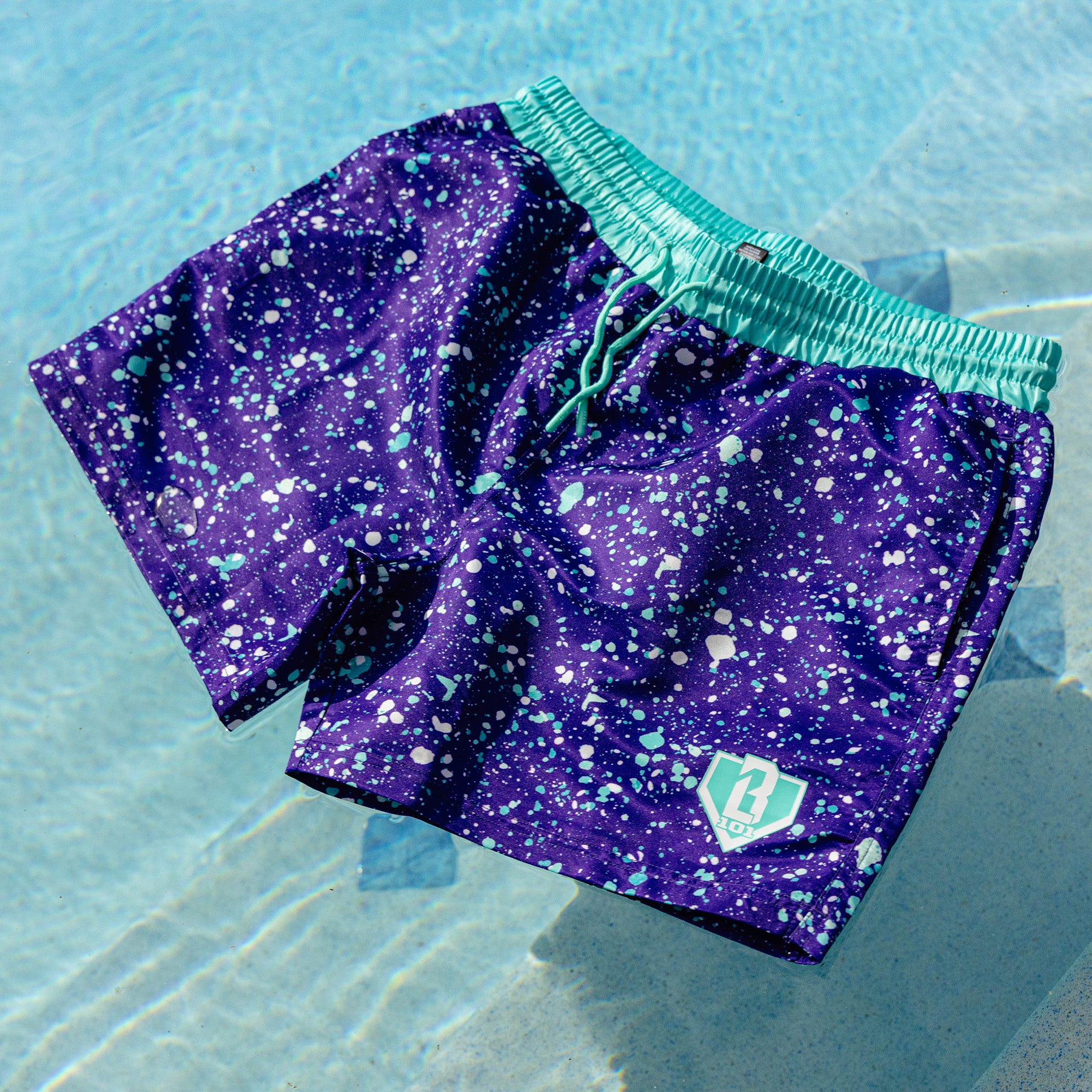 Close-up of BL101 purple splatter swim trunks showing the teal built-in compression liner.