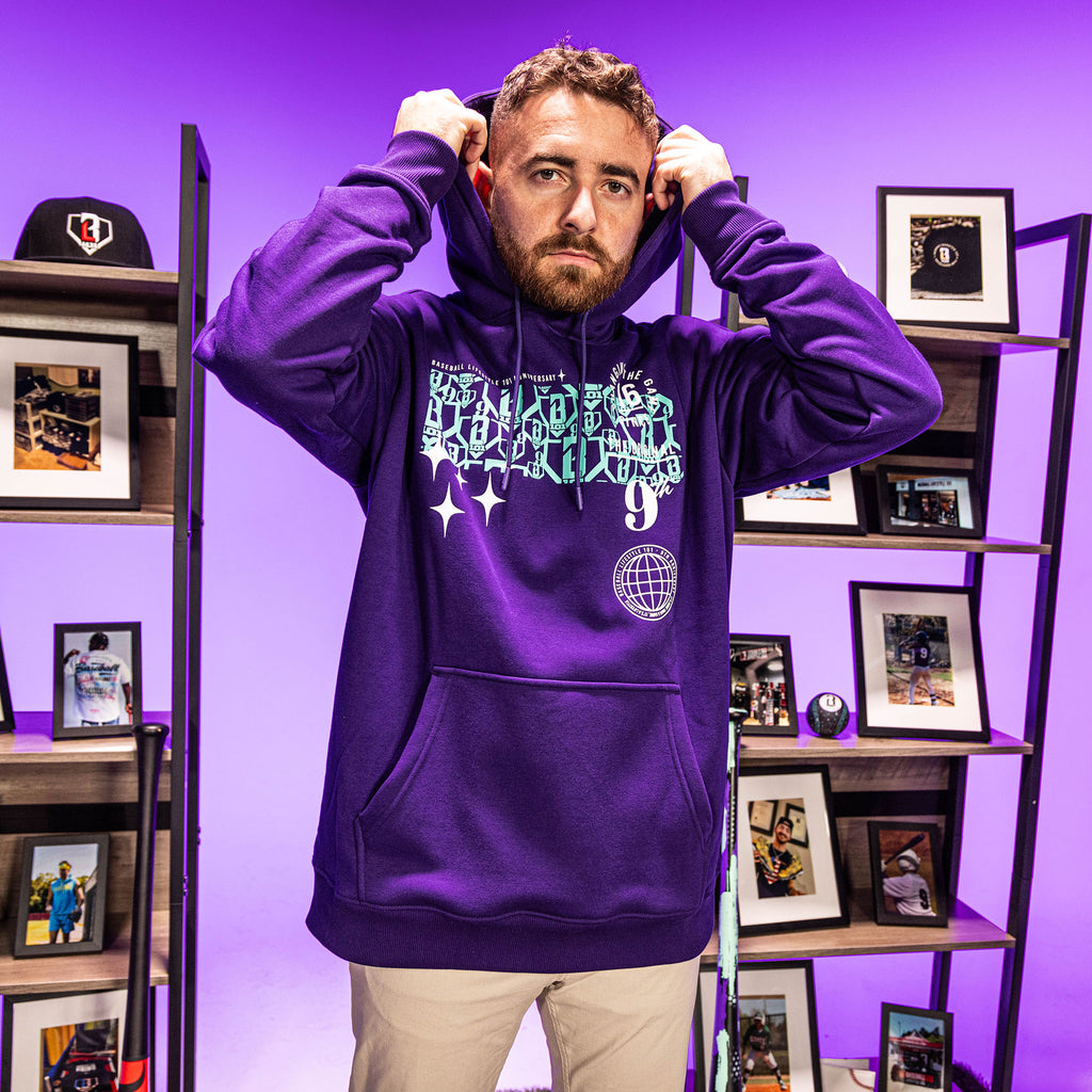 Man wearing a purple hoodie with blue BL101 9th anniversary graphic designs in a room with shelves and framed pictures.