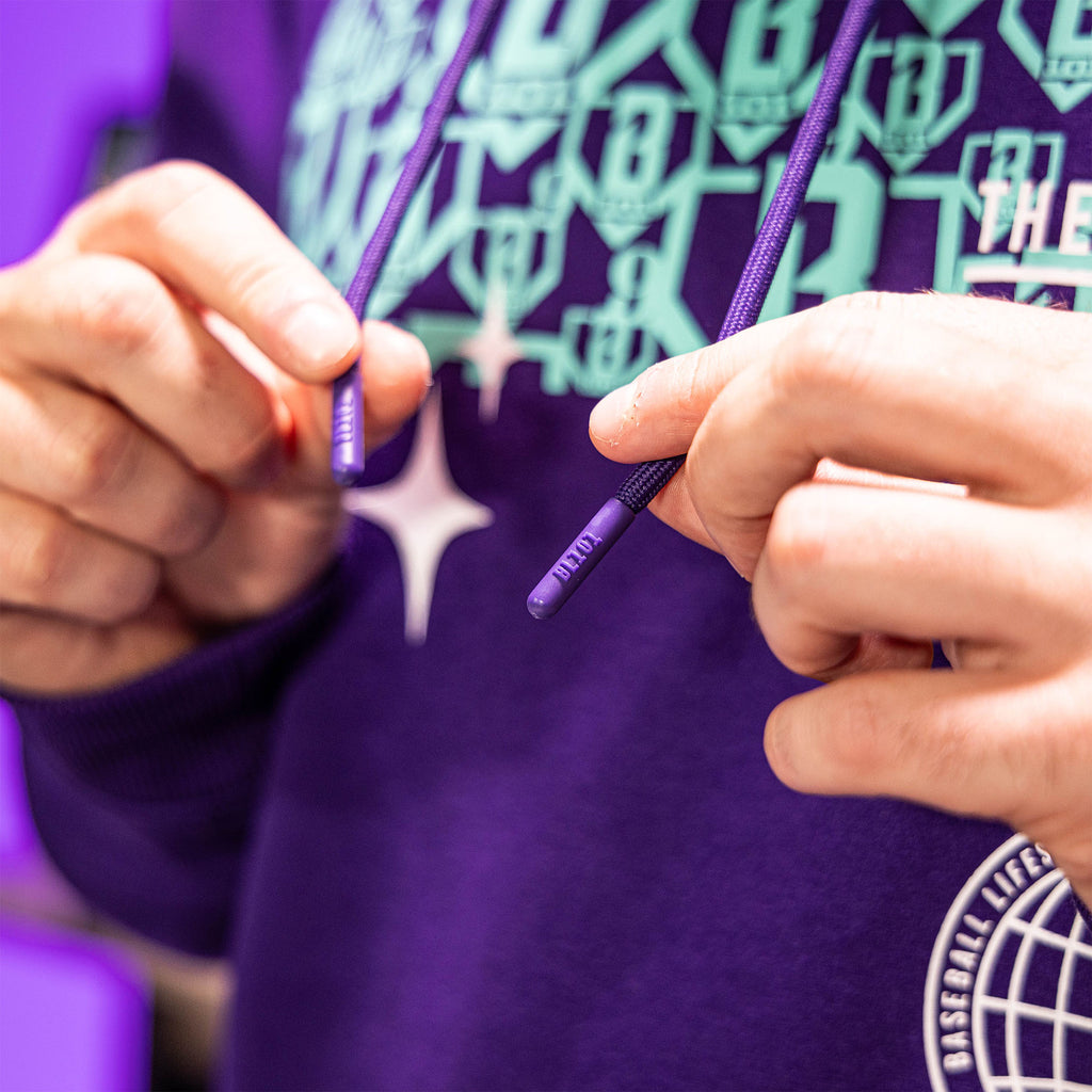 Person wearing a purple hoodie with multiple BL101 logos, holding purple strings with BL101 text on it.