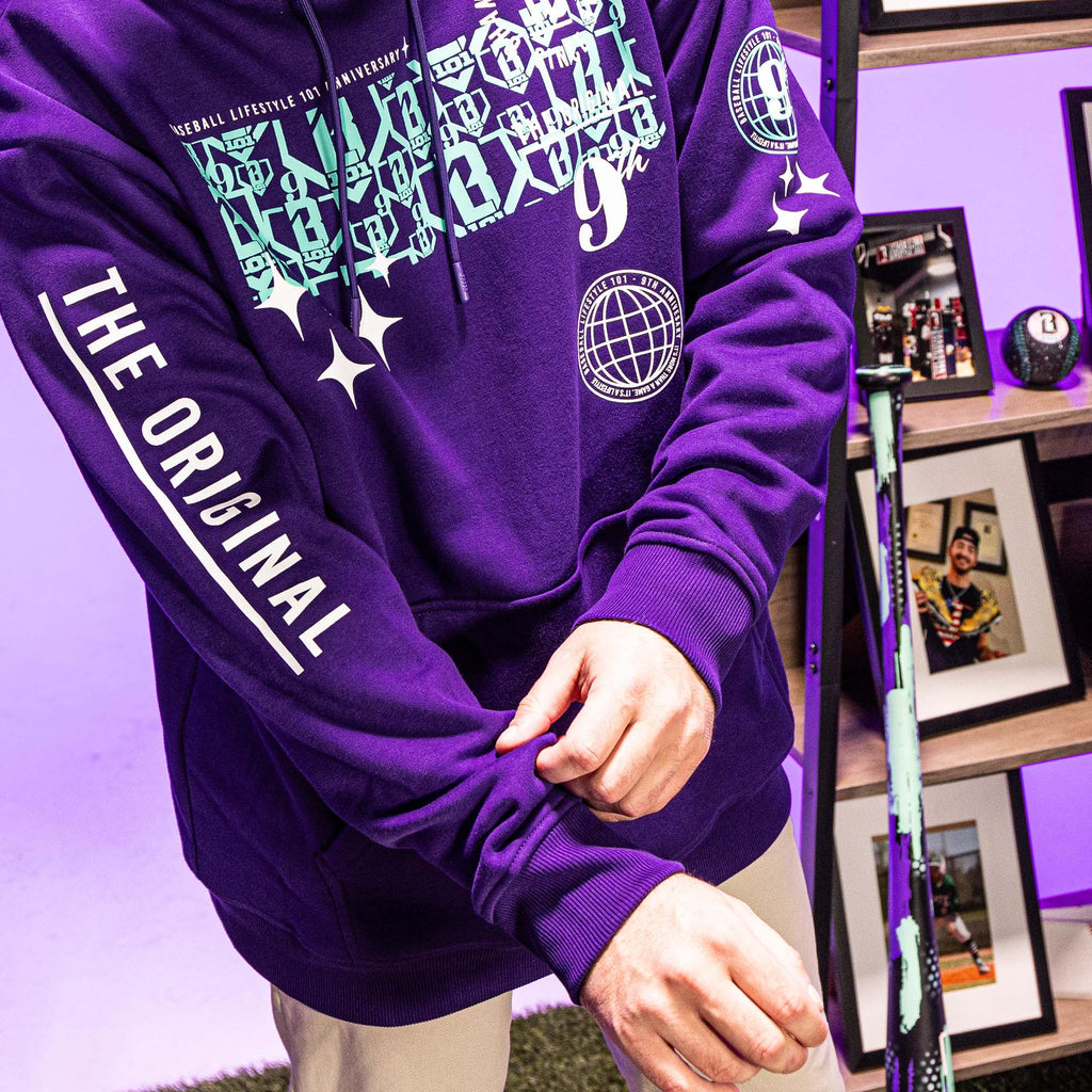 Purple hoodie with text and graphics worn by a person, with a blurred indoor background.