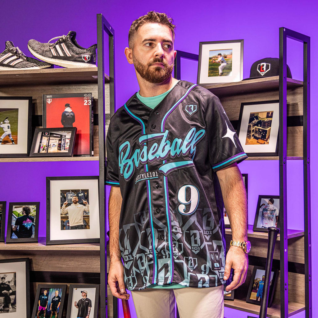 Man wearing black baseball jersey with blue and purple accents and blue 'Baseball Lifestyle 101' text in front of picture frames