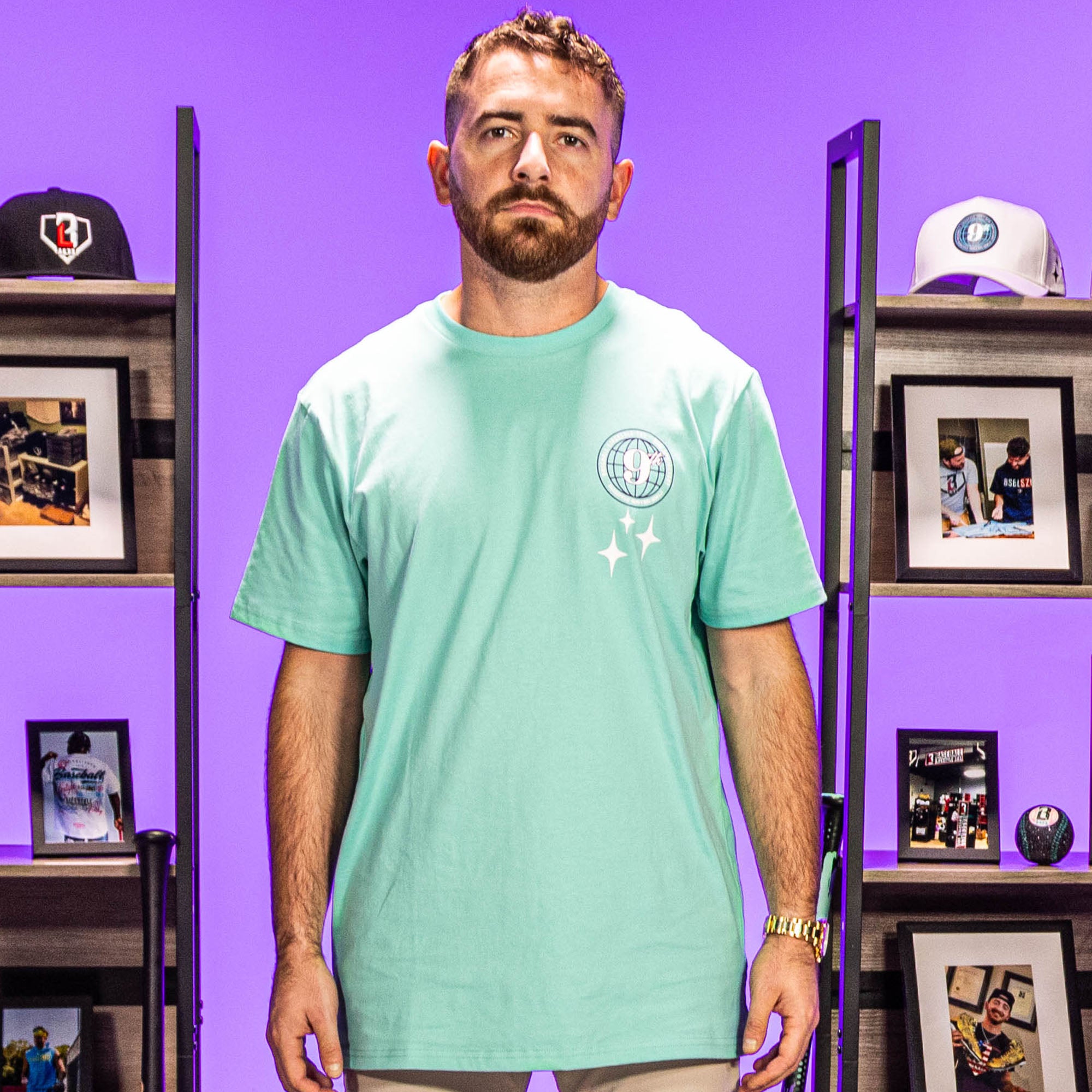 Man wearing Mint green t-shirt with a 9th anniversary Baseball Lifestyle 101 logo and stars in a room with shelves and framed pictures.