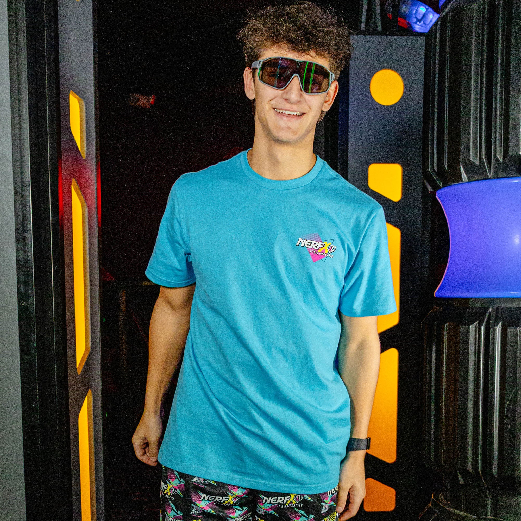 Person wearing a blue t-shirt with a 'NERF' logo in front of colorful background
