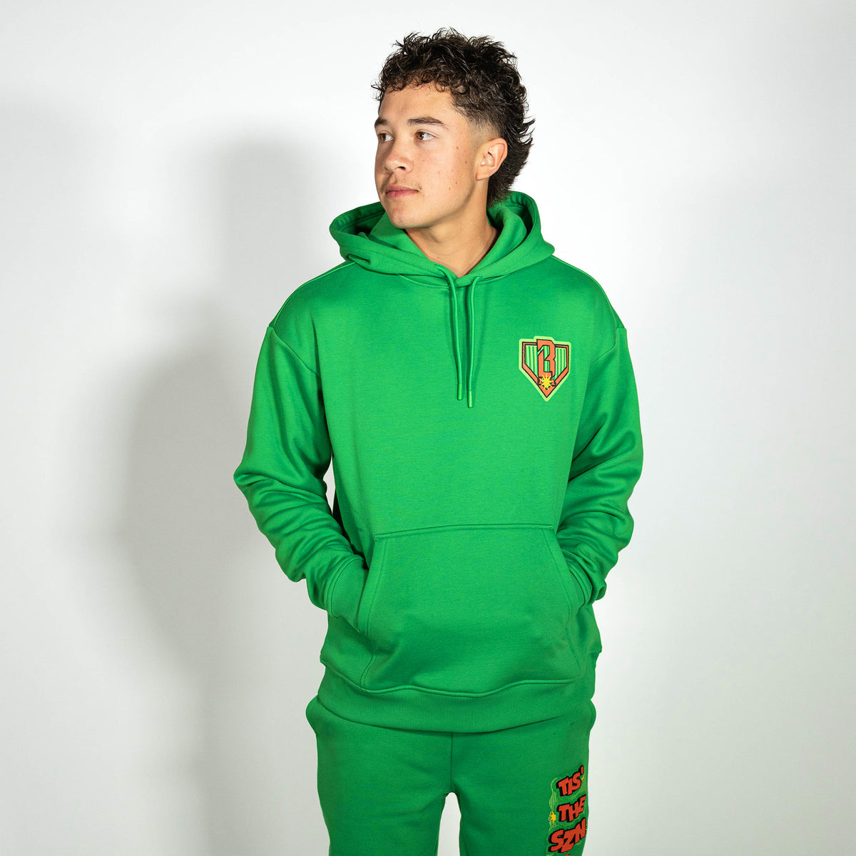 Adult model wearing green hoodie with "Tis The SZN" design