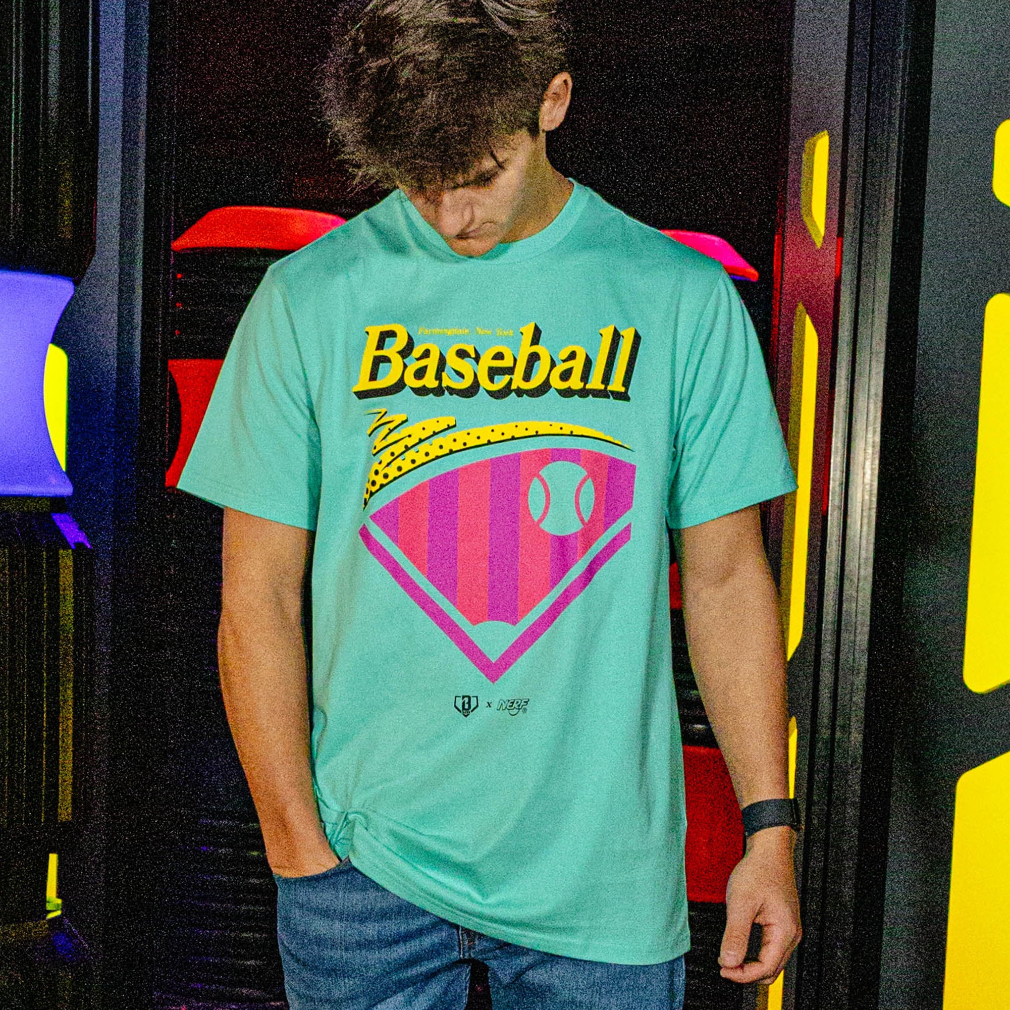 Person wearing a teal t-shirt with 'Baseball' graphic design in front of colorful background