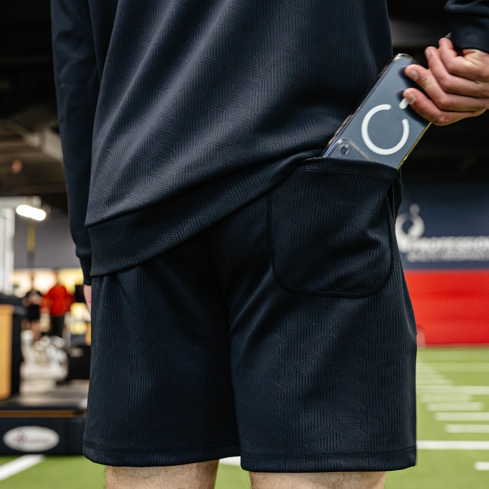 Person wearing dark athletic shorts with a phone case featuring a logo on a sports field.