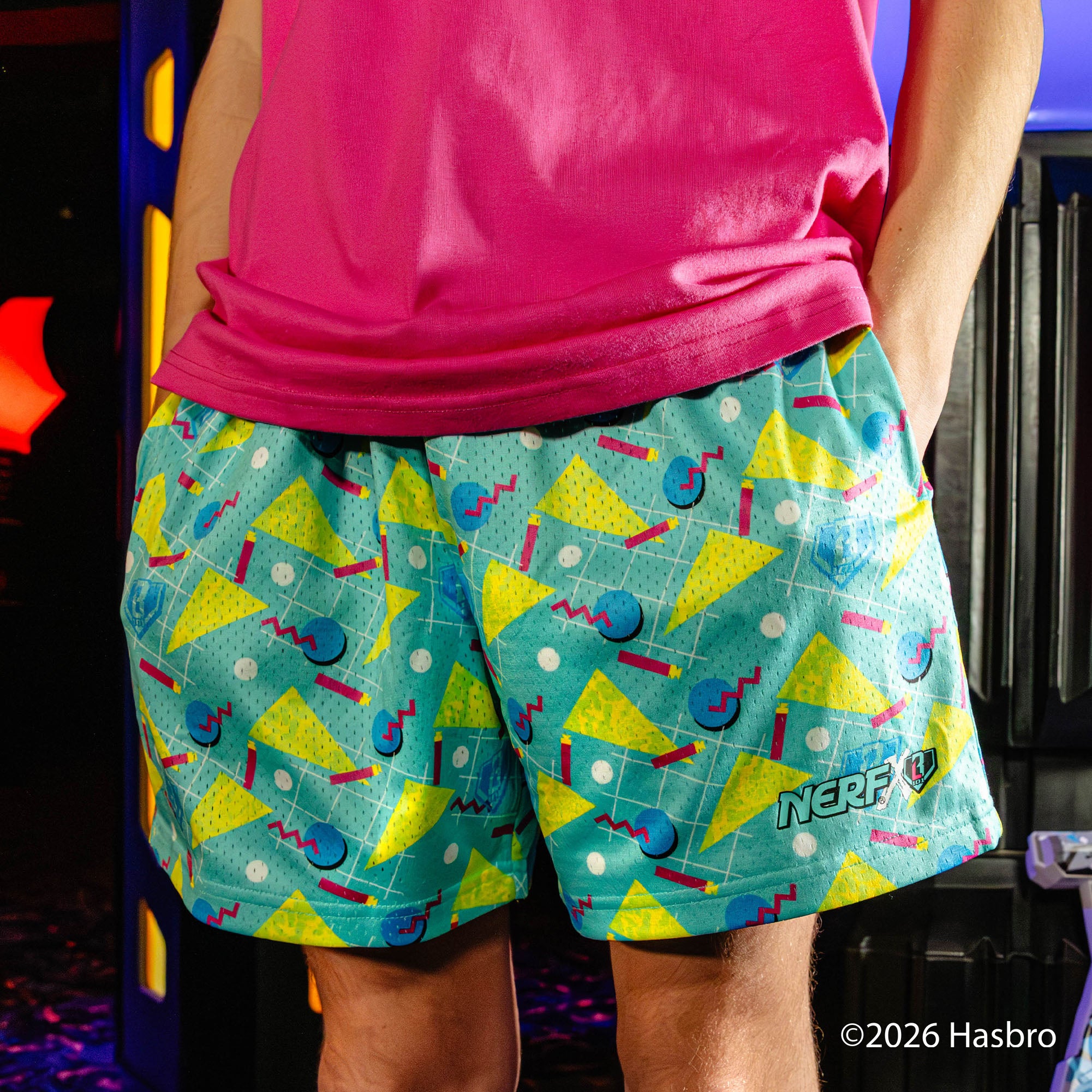 Person wearing colorful shorts with geometric pattern and 'NERF' branding, standing in front of a blurred background.