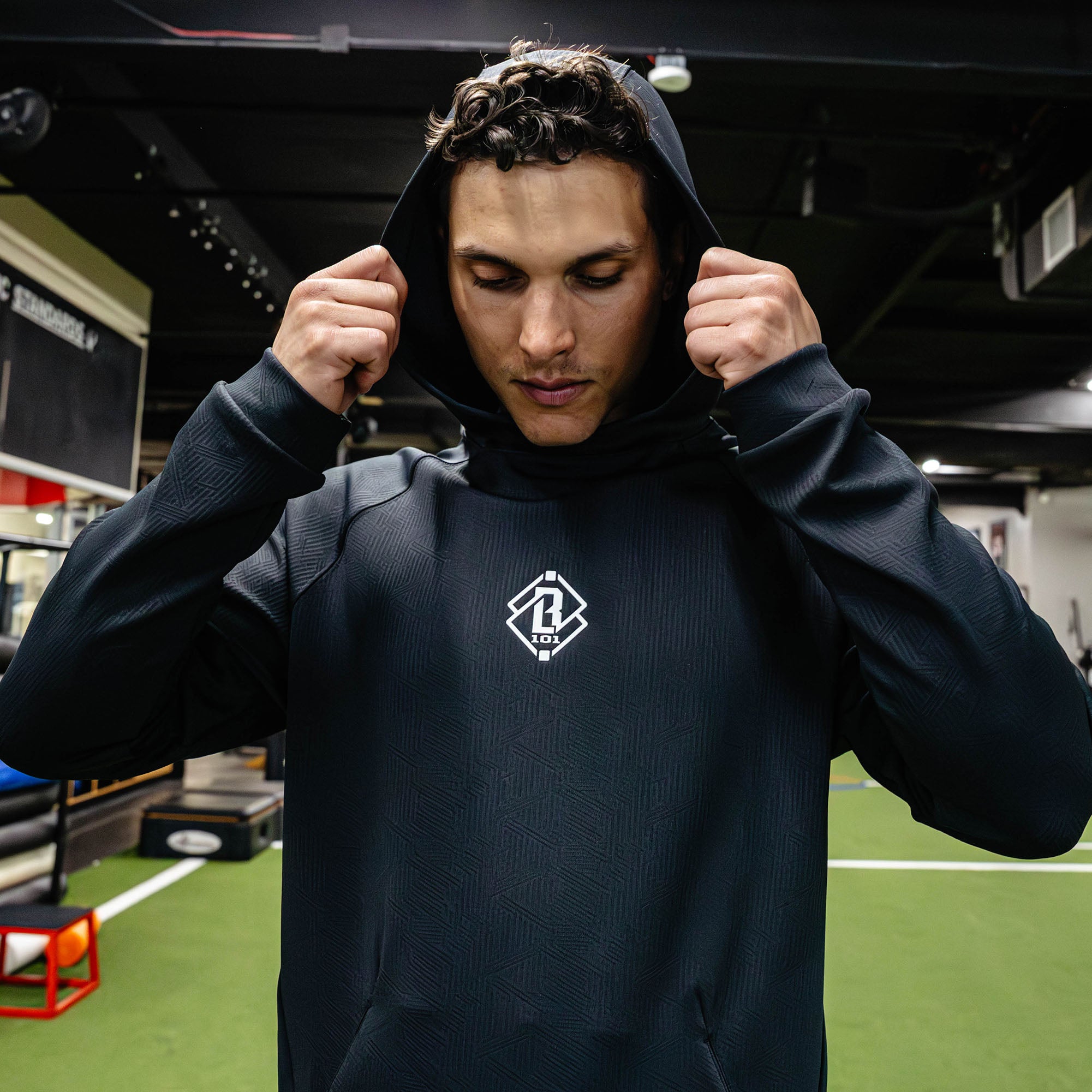 Person wearing a dark hoodie with a logo in an indoor sports facility