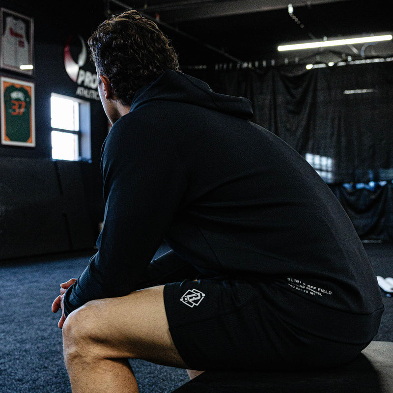 Person sitting on a bench in a gym setting wearing black athletic clothing with logos.