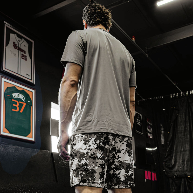 Person wearing a gray t-shirt and camouflage shorts in a locker room setting.