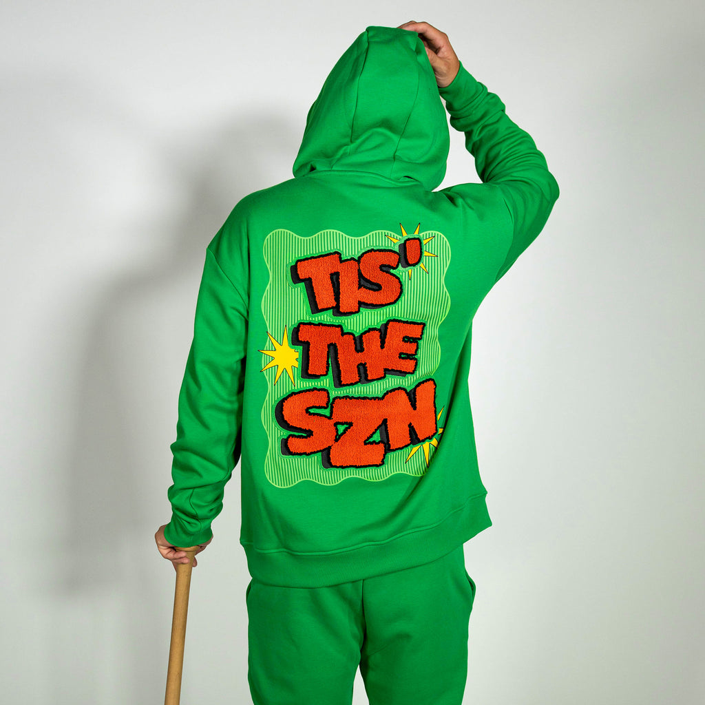 Adult model wearing green hoodie with "Tis The SZN" design