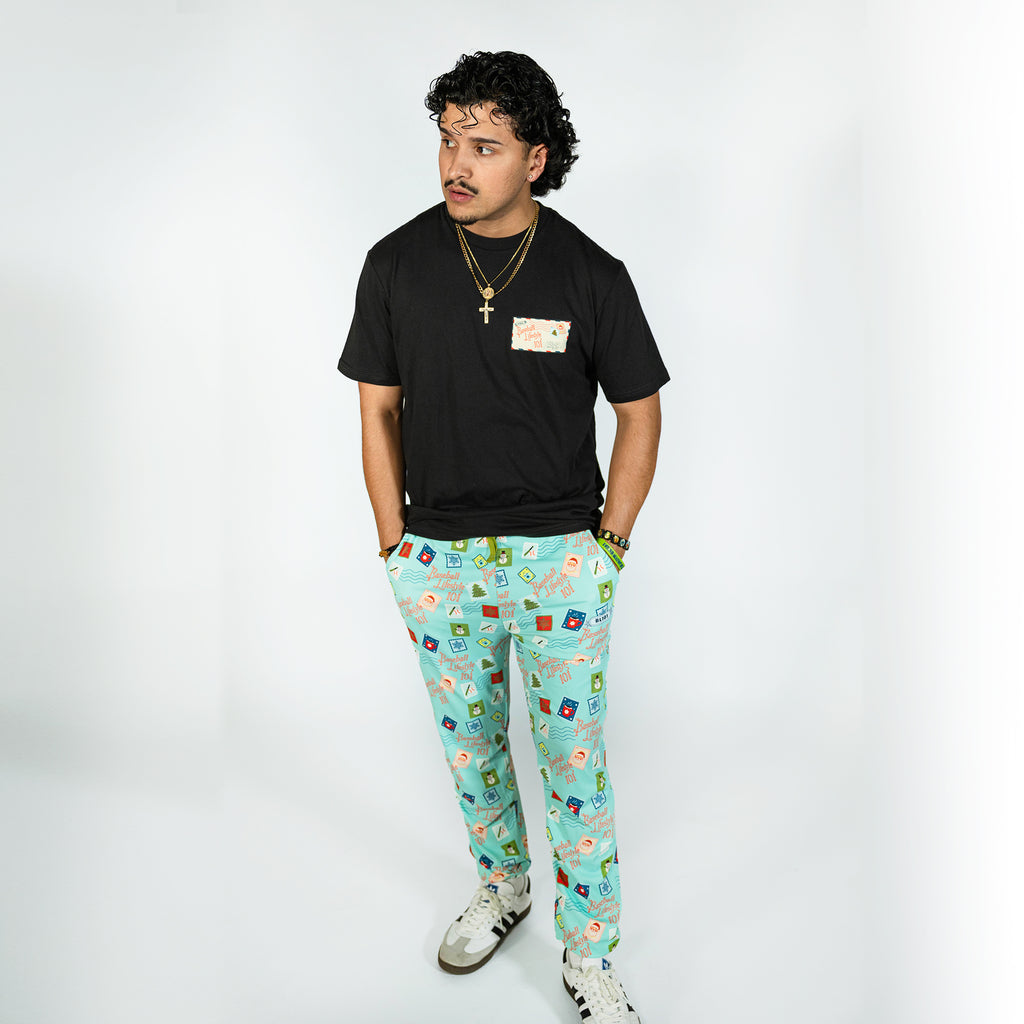 Adult model wearing teal pajama pants with "Holiday Stamps" design
