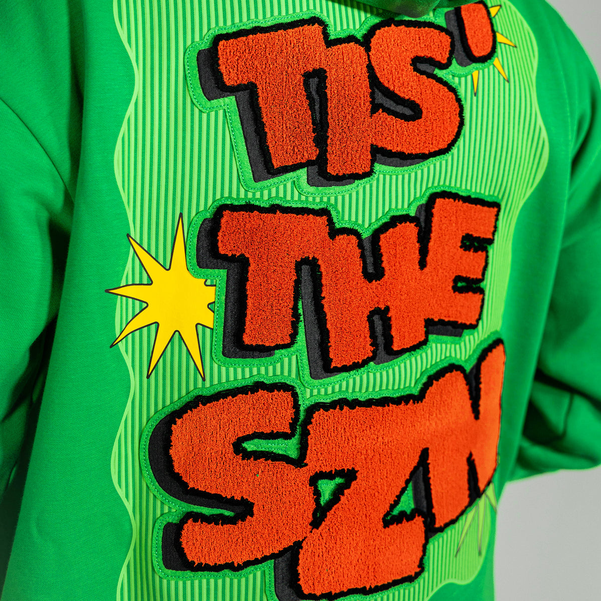 Adult model wearing green hoodie with "Tis The SZN" design