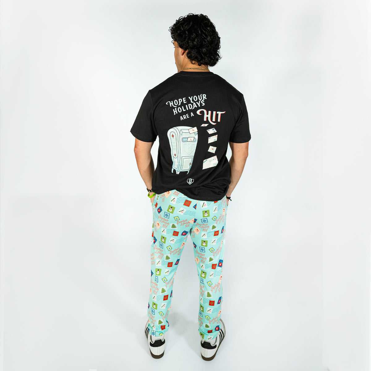 Adult model wearing teal pajama pants with "Holiday Stamps" design