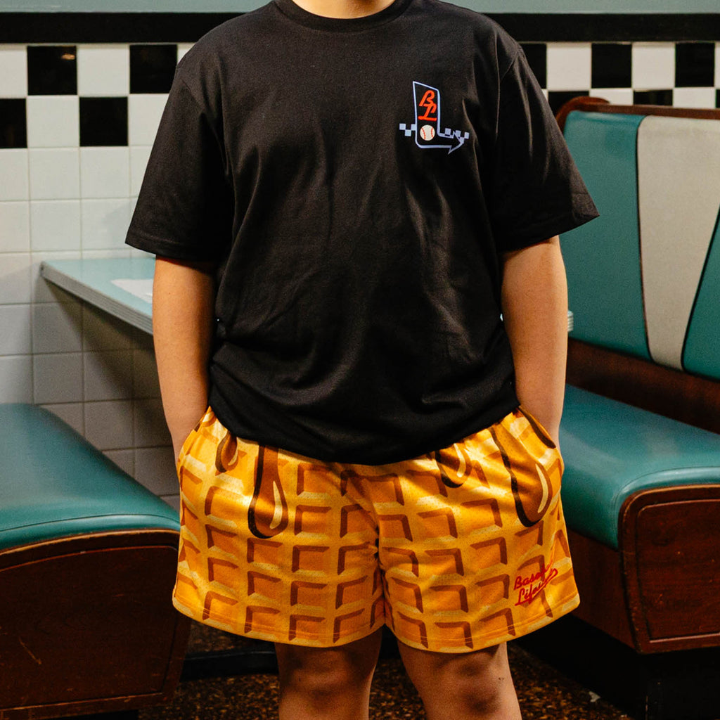 Person wearing a black t-shirt with BL101 logo and waffle shorts in a retro setting.