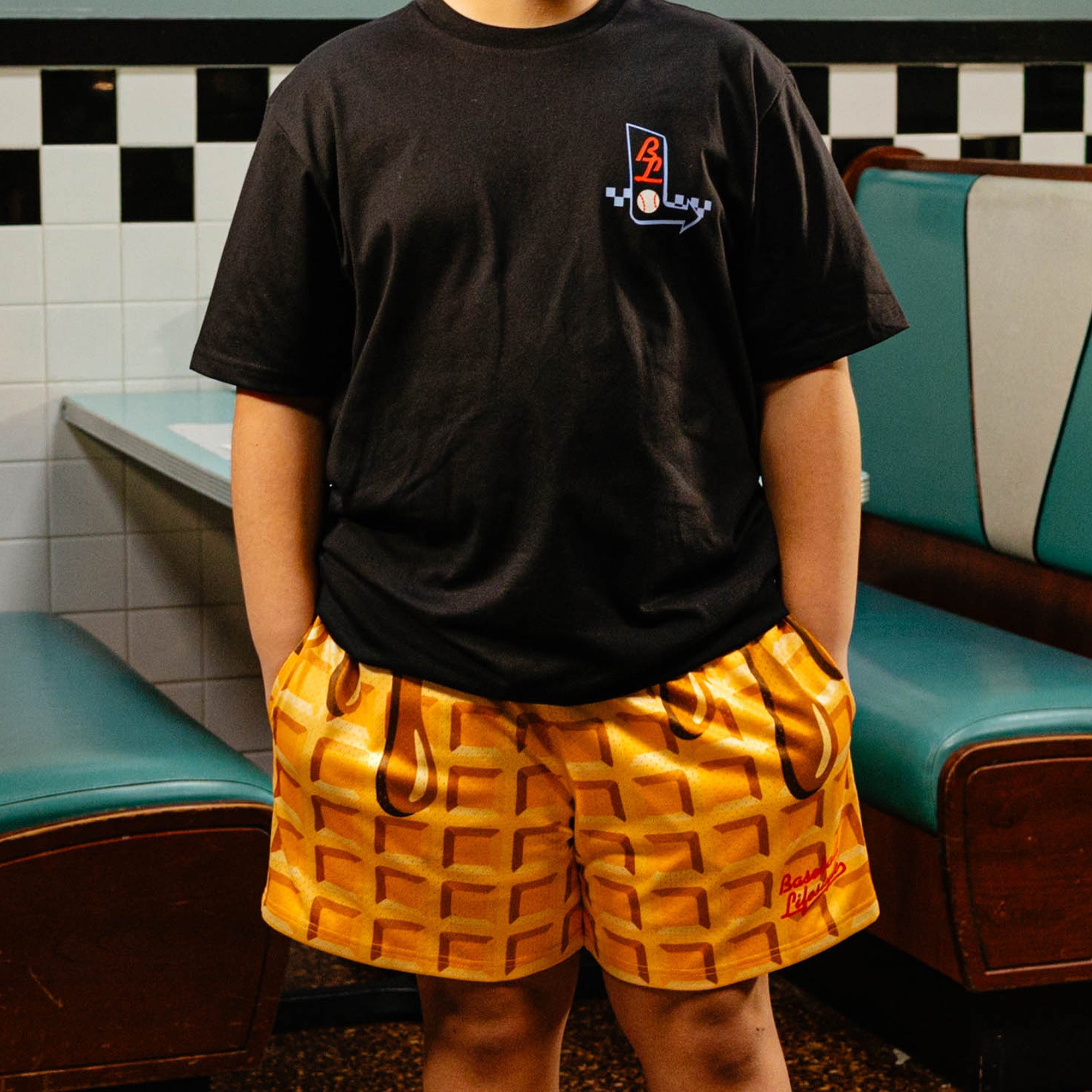 Person wearing a black t-shirt with BL101 logo and waffle shorts in a retro setting.
