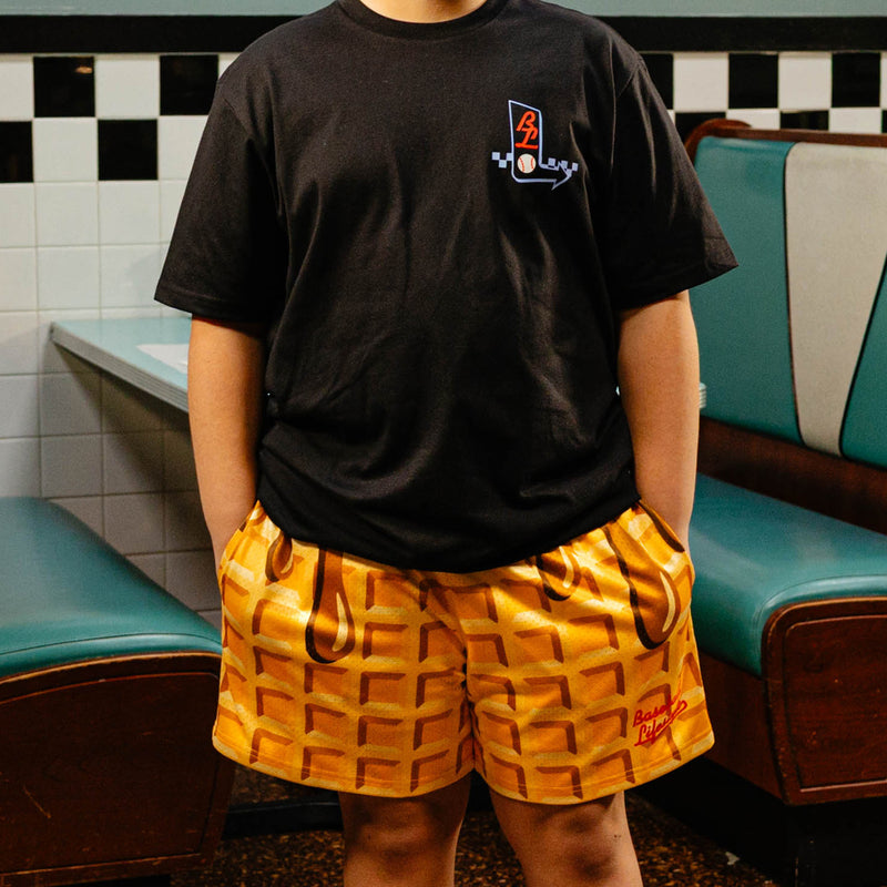 Person wearing a black t-shirt with BL101 logo and waffle shorts in a retro setting.