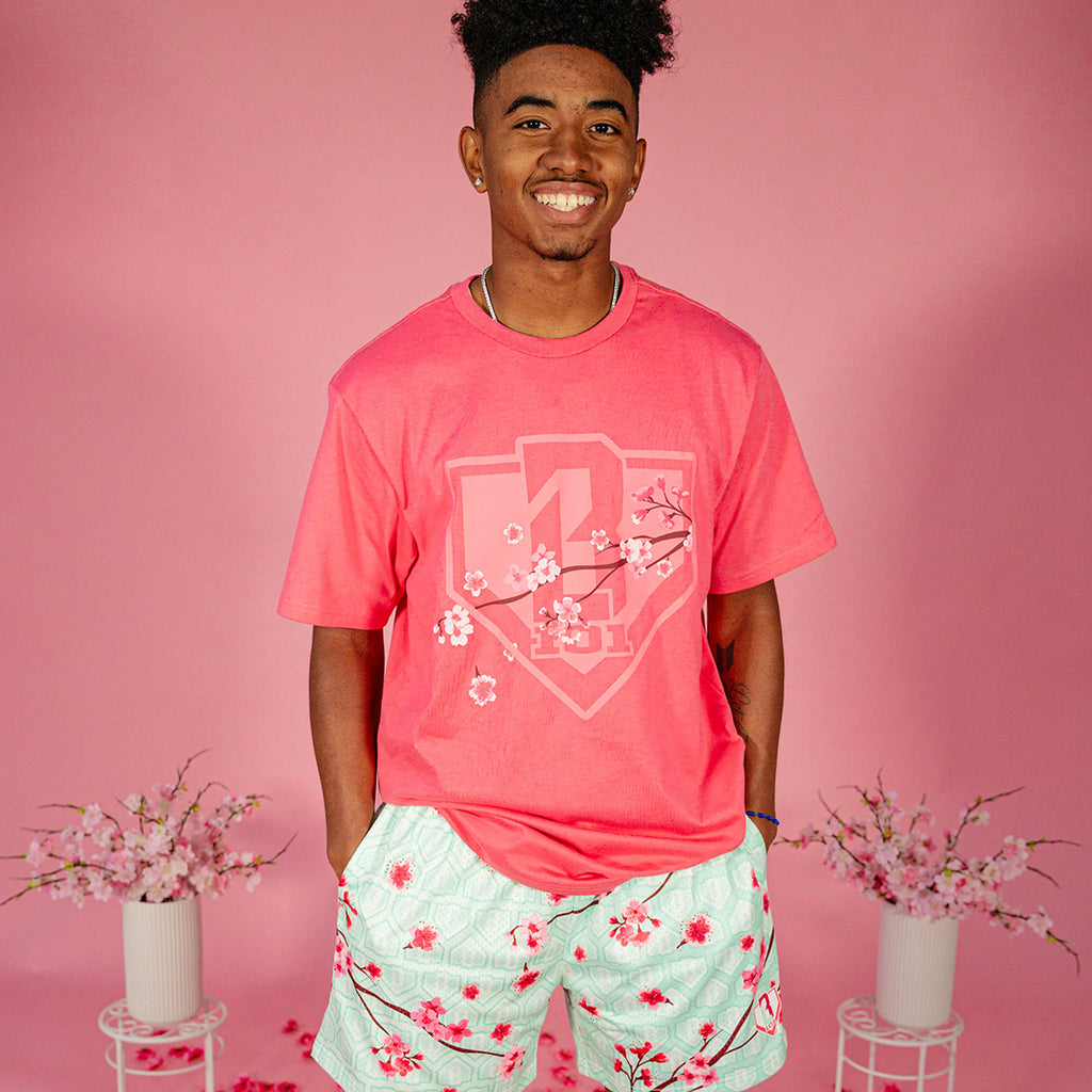 Male model wearing a pink BL101 cherry blossom shield tee and mint green BL101 cherry blossom mesh shorts against a pink background, front view