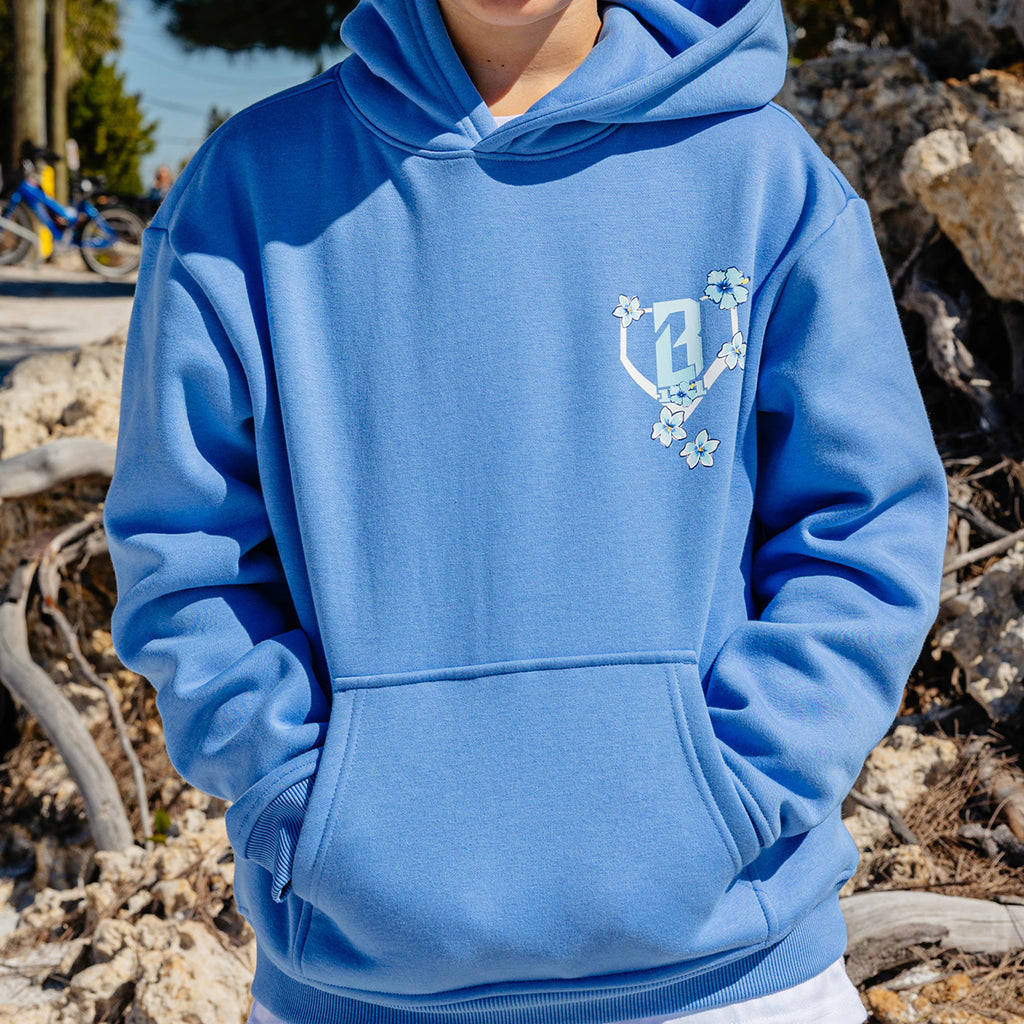 Person wearing a blue hoodie with a floral BL101 logo on a natural background