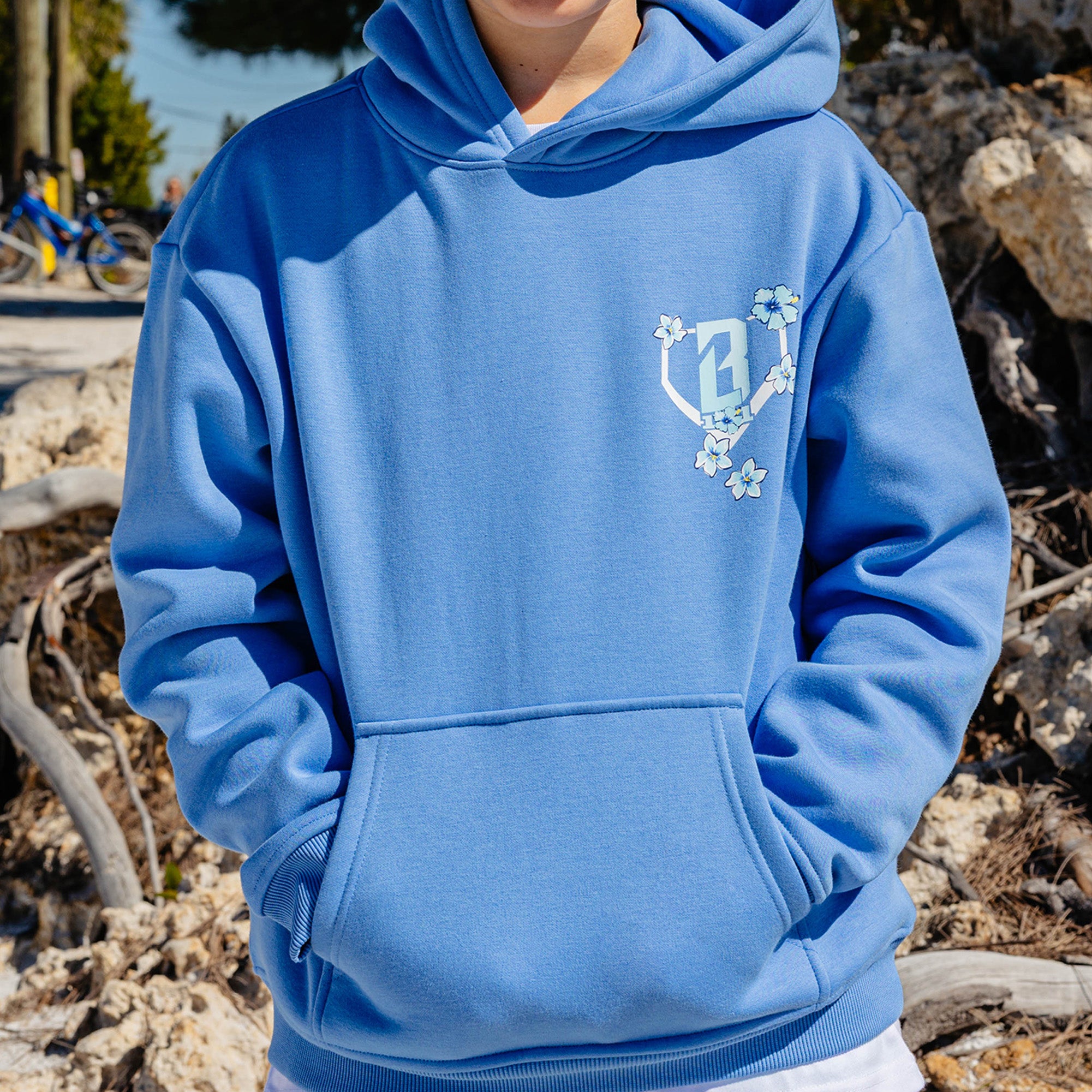Person wearing a blue hoodie with a floral BL101 logo on a natural background