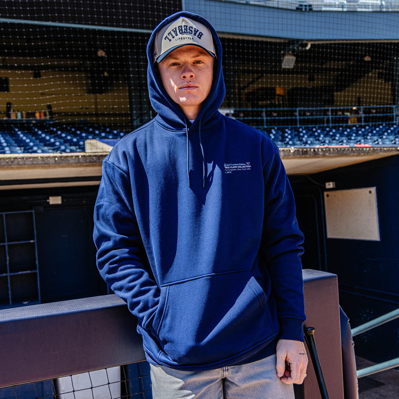 Person wearing a blue hoodie and cap standing in an empty stadium.