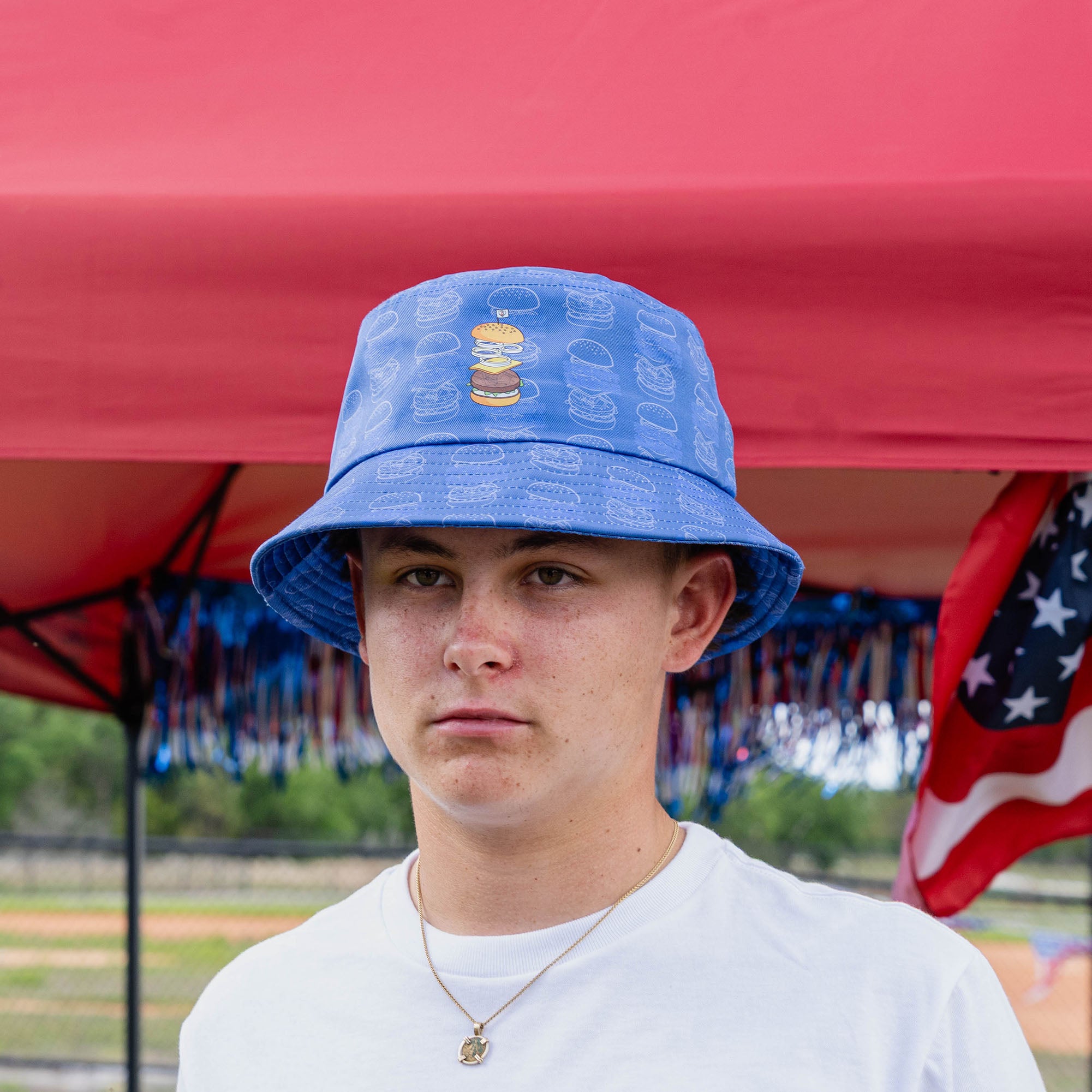 Back view of blue bucket hat with allover burger line art pattern worn by young male model outdoors