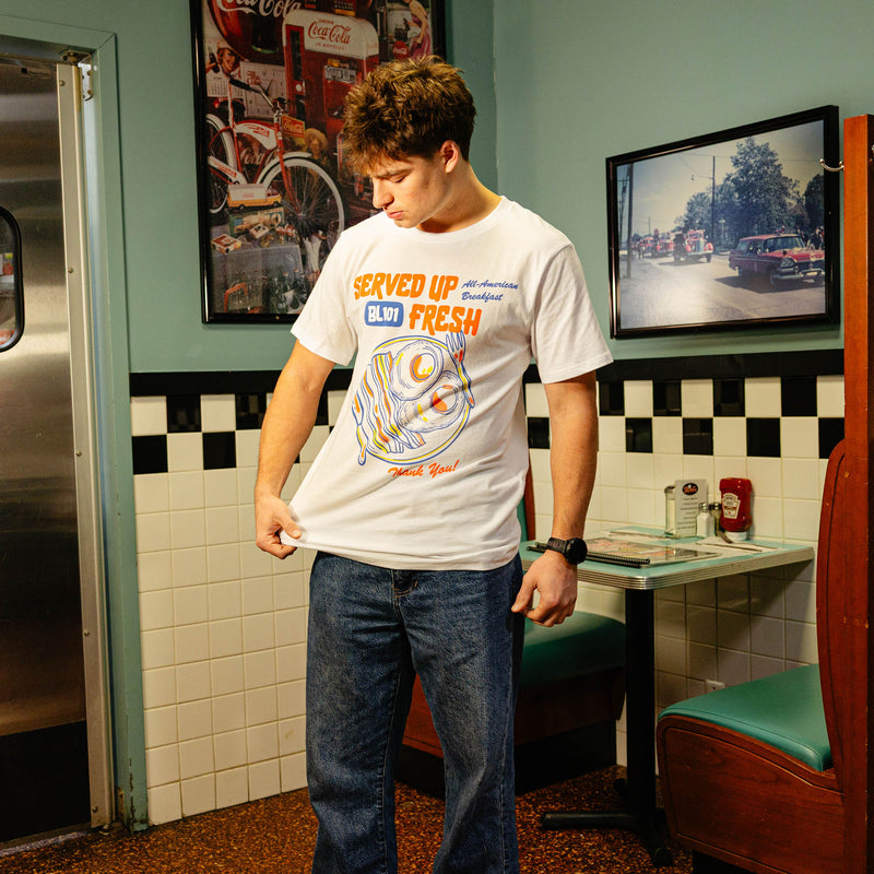 Person wearing white t-shirt with a bacon and egg graphic and 'Served Up BL101 Fresh' text 