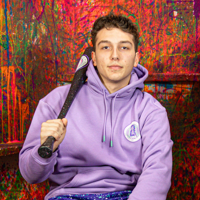 Person wearing a purple hoodie with a small BL101 logo holding a baseball bat against a colorful abstract background