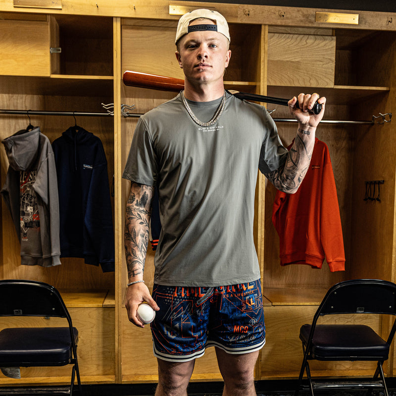 Man holding a baseball bat and ball in a locker room.